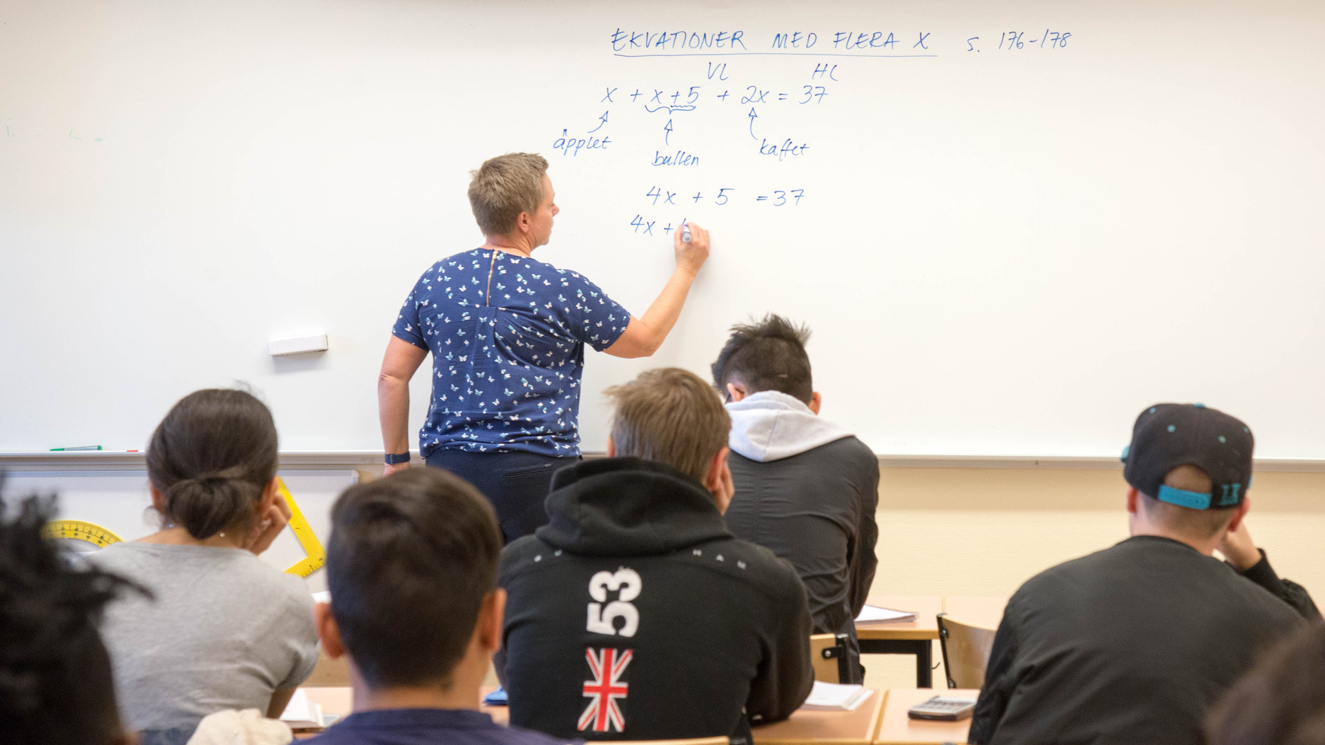 En lärare skriver på whiteboard i ett klassrum.